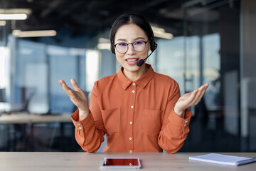 Asian businesswoman wearing headset conducting an online meeting in a modern office setup....