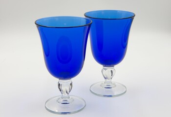 Set of two blue glass goblets on a white table with its own unique design