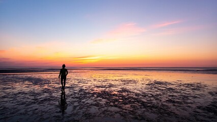 Young person stands on a serene tropical beach with a golden sunset in the background