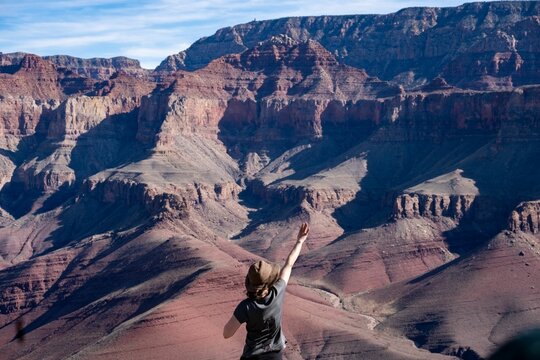 Person stands in front of a stunning view of the Canyon, his arm raised in a gesture of admiration