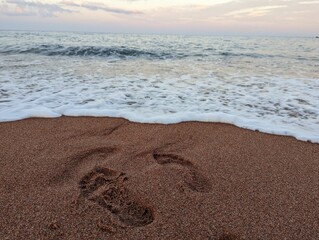 Foot prints made in the sand of a beach, illuminated by the fading light of the setting sun