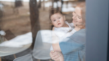 Fototapeta premium View through the window of a red-haired Caucasian woman holding her little son. 