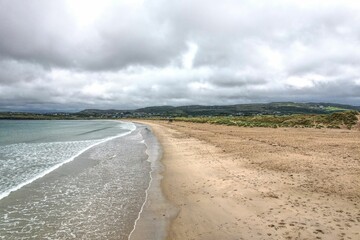 Aerial view of a sandy beach and tranquil sea surrounded by rolling hills in the distance
