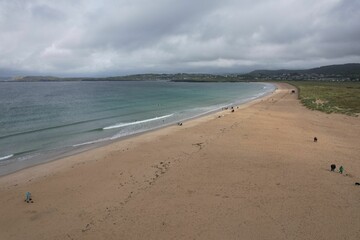 Aerial view of a sandy beach and tranquil sea surrounded by rolling hills in the distance