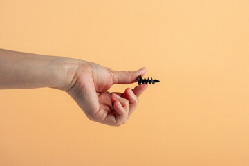 A black screw in hand on cream background.