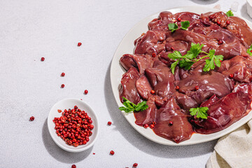 Raw chicken liver on stone background. Fresh ingredients ready for cooking, parsley, red pepper
