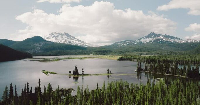Landscape scene of pine trees by Sparks Lake with snowy mountains range with blue cloudy sky