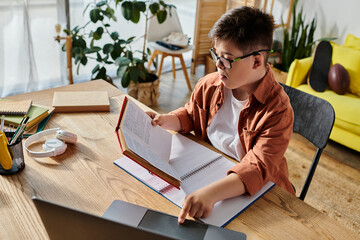 adorable boy with Down syndrome engrossed in laptop and book at table.