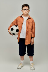 little boy with Down syndrome with glasses holds a soccer ball.