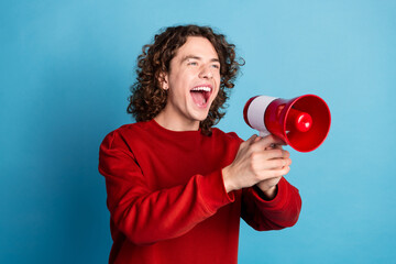 Photo of attractive funny guy wear red sweater yelling lous speaker emtpy space isolated blue color...