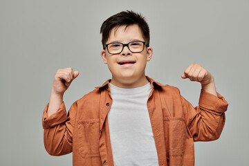 little boy with Down syndrome flexing his arms proudly against a gray background. © Bliss