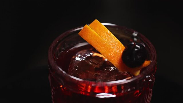 Overhead view on classic negroni drink garnished with orange peel zest and black olive on skewer. Decorating details of old fashioned alcohol cocktail chilled with ice cube in glass.