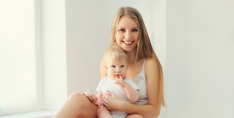 Happy smiling young mother playing with baby in white room at home