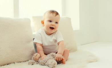 Happy cute little baby playing with teddy bear toy in white room at home