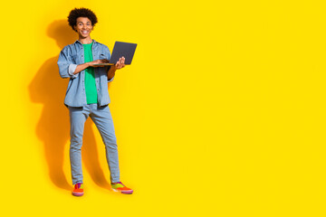 Full size portrait of nice young man laptop empty space wear denim shirt isolated on yellow color background