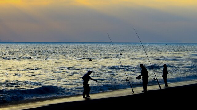 Group of people enjoying a leisurely afternoon of fishing off the beach at sunset