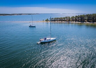 two sail boats floating in the middle of an ocean near some trees