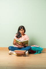 Indian asian school girl in casual wear reading book while sitting on floor