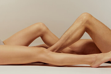 Male and female legs against warm grey background. Skincare products, focusing on the smooth and...