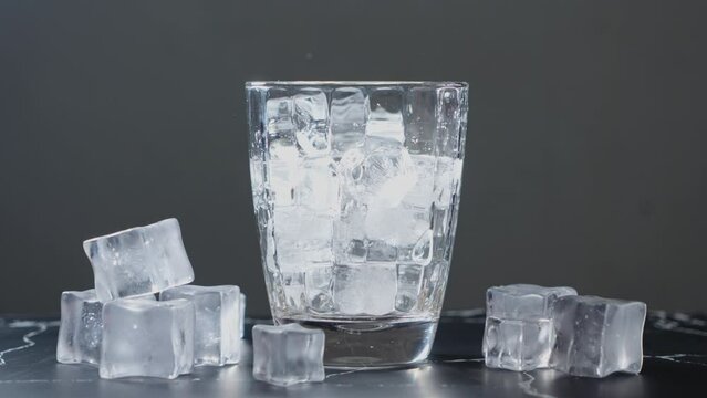 Throw ice cubes in empty glass. Ice Cubes falling down in empty transparent glass. Make a fresh drink. Footage b roll scene 4k. Slow motion.