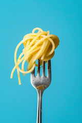 Fork with twirl of spaghetti noodles on blue background. Delicious pasta serving, close up