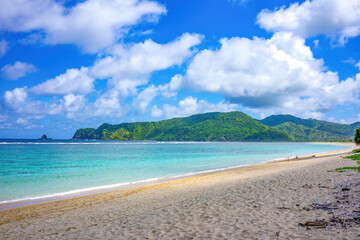 Stunning summer view of the pristine beach and turquoise waters in Lombok, Indonesia, with lush green hills under a bright blue sky.