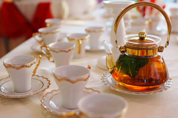 Classic white and gold tea set and glass teapot on the served table. Dishes for tea drinking.