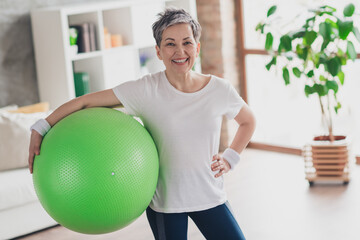 Photo of nice pensioner woman hold pilates ball sportswear home exercising routine living room...