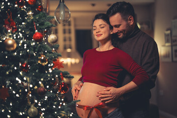 A happy young adult couple in a warm embrace expecting a baby on Christmas Eve