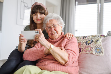 Grandmother with cute girl taking selfie with smartphone. Portrait of an elderly woman spending time with granddaughter.