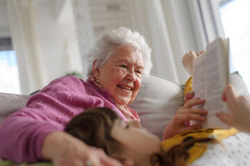 Cute girl lying head on gradmother knees. Portrait of an elderly woman spending time with granddaughter.