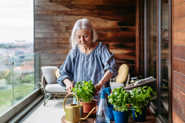 Portrait of beautiful mature woman taking care of plants on balcony. Spending free weekend at home.