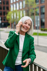 Mature businesswoman phone calling on smartphone, going on business meeting in the city. Beautiful older woman with gray hair standing on city street.