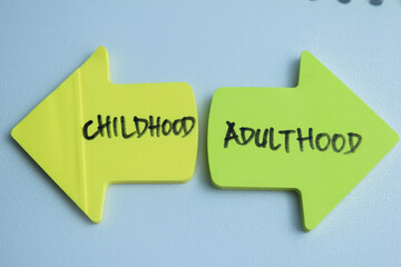 Concept of Childhood or Adulthood write on sticky notes isolated on Wooden Table.