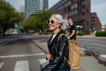Portrait of stylish mature woman with gray hair on city street. Older woman in sunglasses waiting for public transport.
