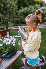 Girl watering flower seedlings in tray, holding metal watering can. Taking care of garden and planting spring flowers.