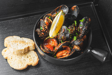 A close-up of a bowl of mussels garnished with parsley and lemon, served with slices of bread on a...