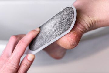 Woman's hands cleaning the heel with pumice in the bathroom.