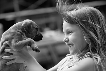 cute cheerful little girl holding boxer puppy up in the air in black in white