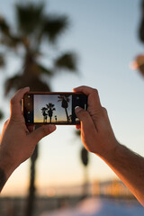 Close up view of male tourist shooting video of beautiful scenery sunset using smartphone camera,...