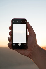 Close up view of male holding modern smartphone with mock up screen against sundown in evening, cropped image of telephone in man's hand with copy space area for your web content or app on display