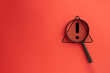 Close-Up View of Warning Triangle Icon Under Magnifying Glass on Red Background: Highlighting Hazard Awareness.