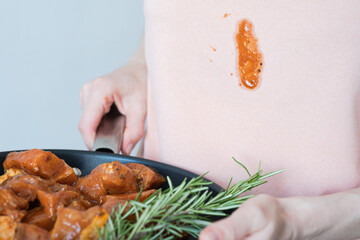 A dirty stain of tomato sauce on pink clothes. Unrecognizable woman holding marinated meat for...