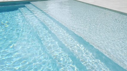 Close up view of swimming pool with clear blue water. Sunlight reflecting sun and creating patterns of light and shadow. Outdoors setting