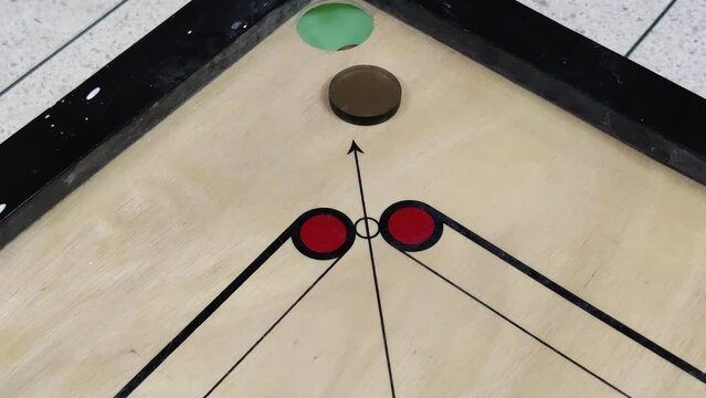 Footage of a carrom board with carrom coins on the board hit with a striker kept at one end of the board