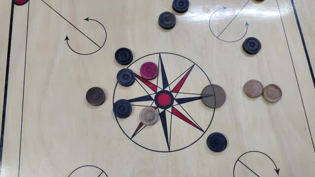 Footage of a carrom board with carrom coins on the board hit with a striker kept at one end of the board