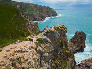 Fototapeta premium Cabo da Roca is the westernmost cape of the Eurasian continent, located in Portugal. A couple stands on a rocky ocean shore.