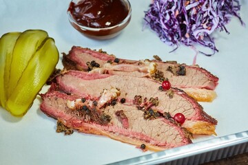 Meat baked in the oven with spices lies in a white container with sliced pickled cucumber, cabbage and ketchup. Meat production