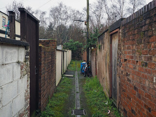 typical narrow back alley in an english city street with brick back yard walls and rubbish on the ground and a bicycle against a wall