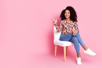 Full length photo of girlish pretty lady dressed print shirt sitting chair showing empty space isolated pink color background